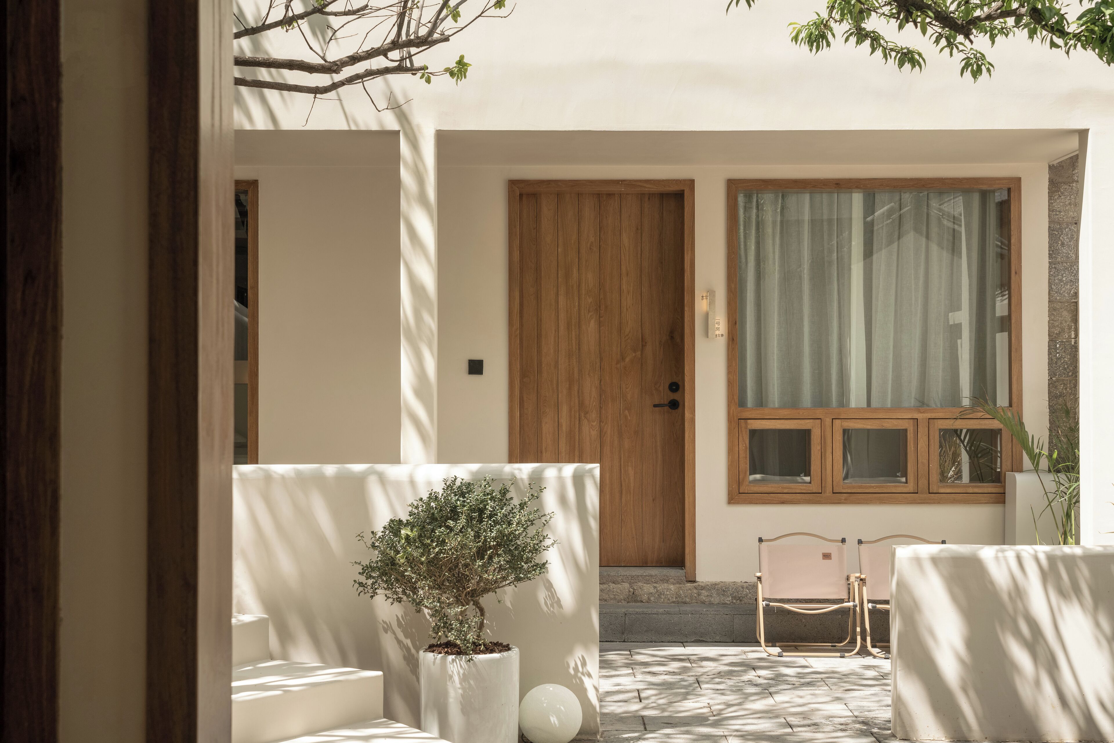 A modern interior with a wooden door, a window with curtains, a potted plant, and two chairs.