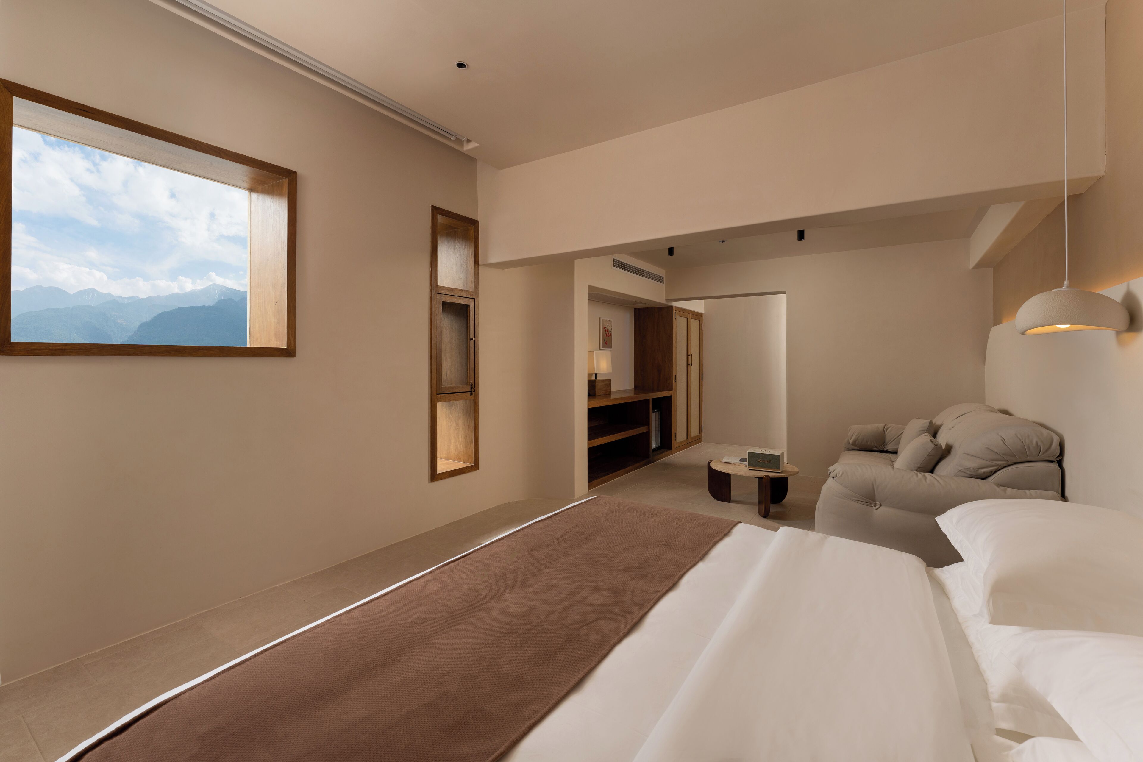 Un dormitorio moderno con una cama grande, un sofá, un escritorio y vistas a montañas a través de una ventana.