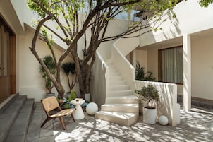 Un espacio exterior moderno con una escalera, plantas en macetas y una silla de madera.
