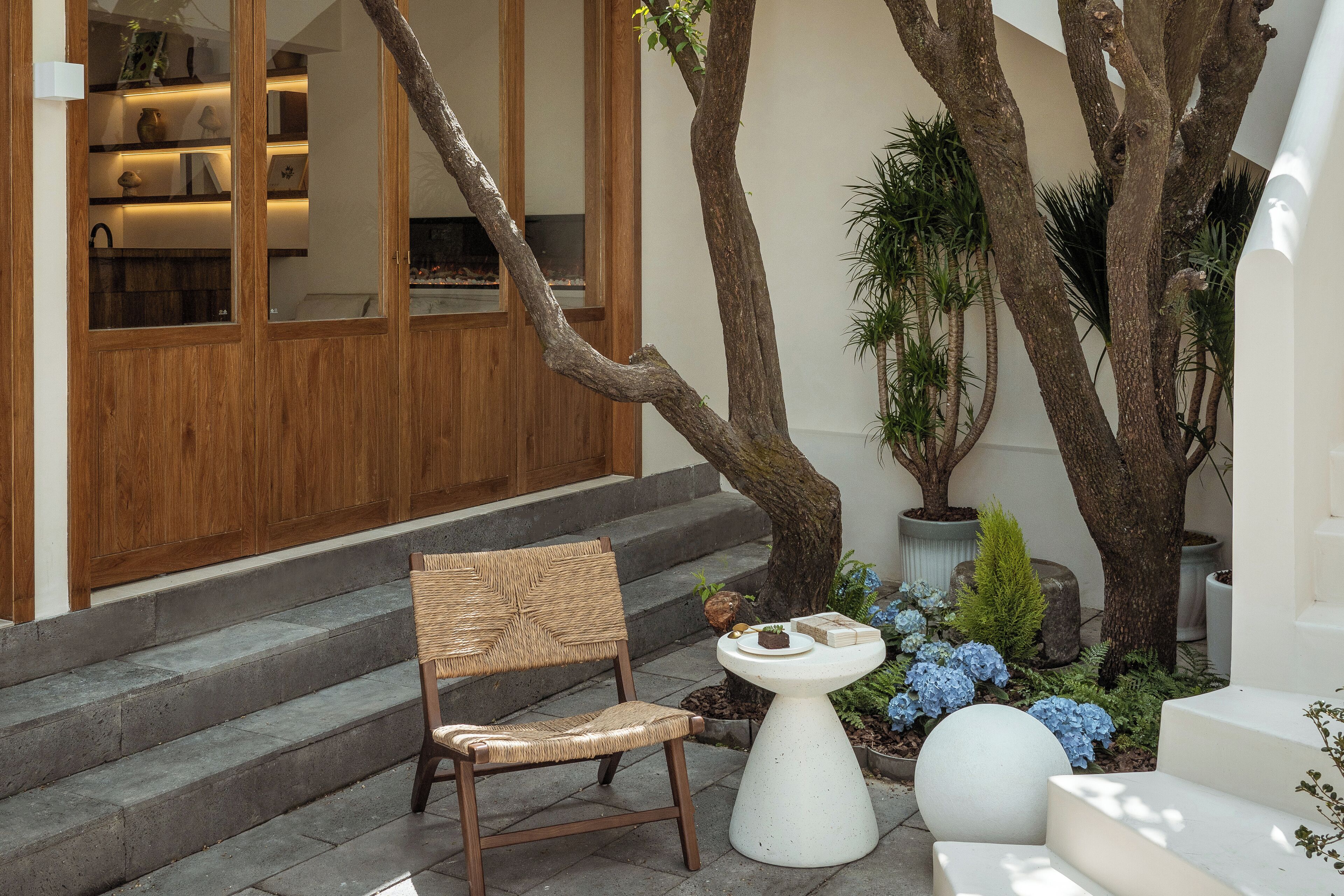 A wooden staircase leading to a room with a large window, a wicker chair, and a small white table with decorative items.