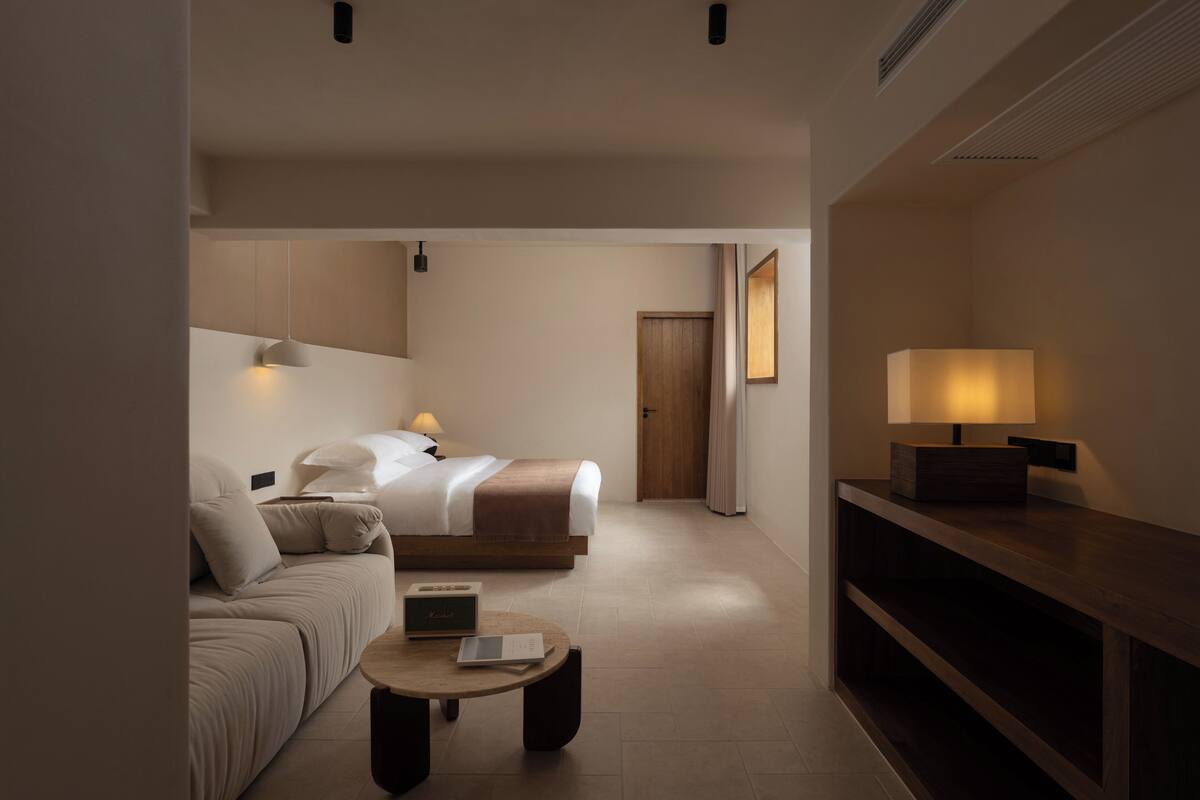 Una habitación de hotel moderna con una cama, un sofá, una mesita de centro y un mueble para televisión.