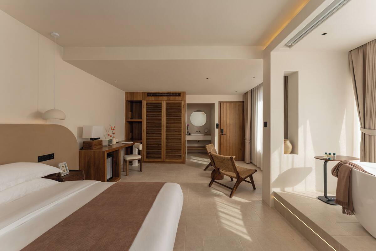 Una habitación de hotel moderna con una cama grande, un escritorio, una silla, un sofá y un baño visible al fondo.