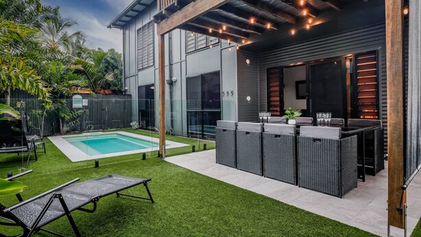 Un patio moderno al aire libre con piscina, sillas de descanso y una zona de bar.