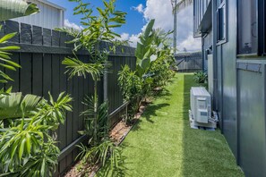 A narrow pathway with artificial grass, flanked by a wooden fence and various tropical plants. - Dolphin Dreamin' with magnesium pool (Agnes Water)