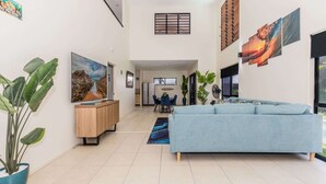 Amplia sala de estar con un sofá azul claro, un escritorio de madera y un comedor al fondo.