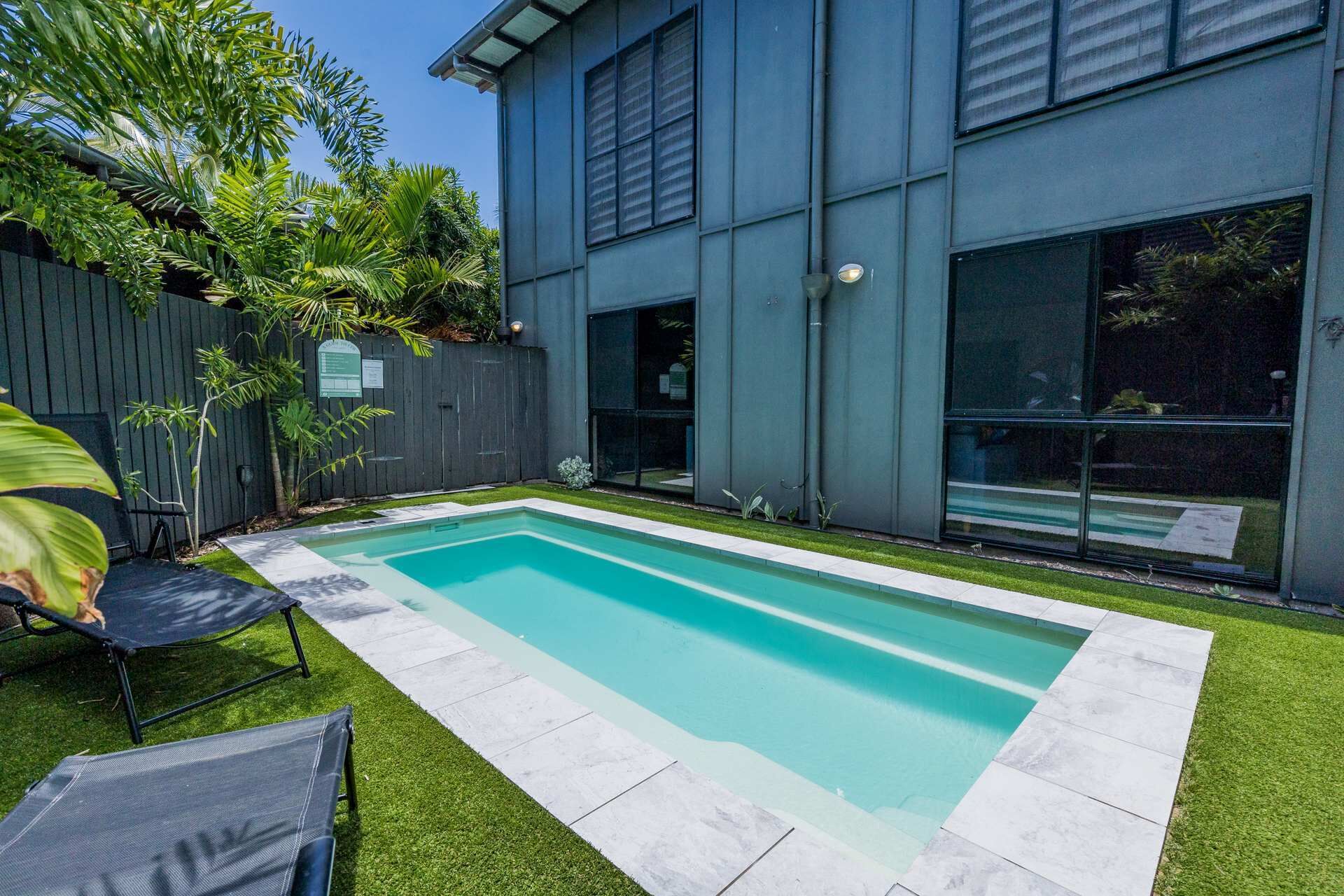 A modern house with a rectangular swimming pool, a wooden fence, and a well-maintained lawn.