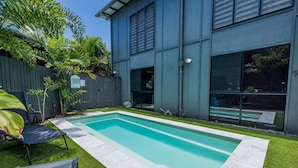 Una casa moderna con una piscina rectangular, un cerco de madera y un césped bien cuidado.