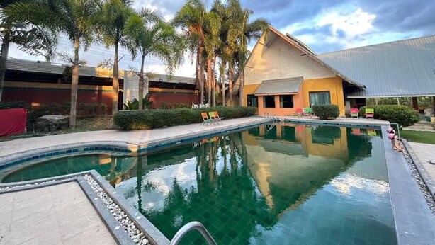 A swimming pool with lounge chairs, palm trees, and a building with a sloped roof. - Petpumok Wangnamkhiao Hotel (Wang Nam Khiao)