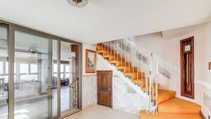 A spacious living area with a large sliding glass door leading to a balcony, a wooden staircase with orange steps, and a marble floor. - Beachfront Home ~ 7 Mi to Cape May! (Villas)