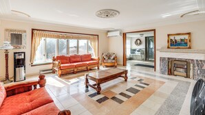 A spacious living room with a large window, a fireplace, a sofa, a coffee table, and a fan. - Beachfront Home ~ 7 Mi to Cape May! (Villas)