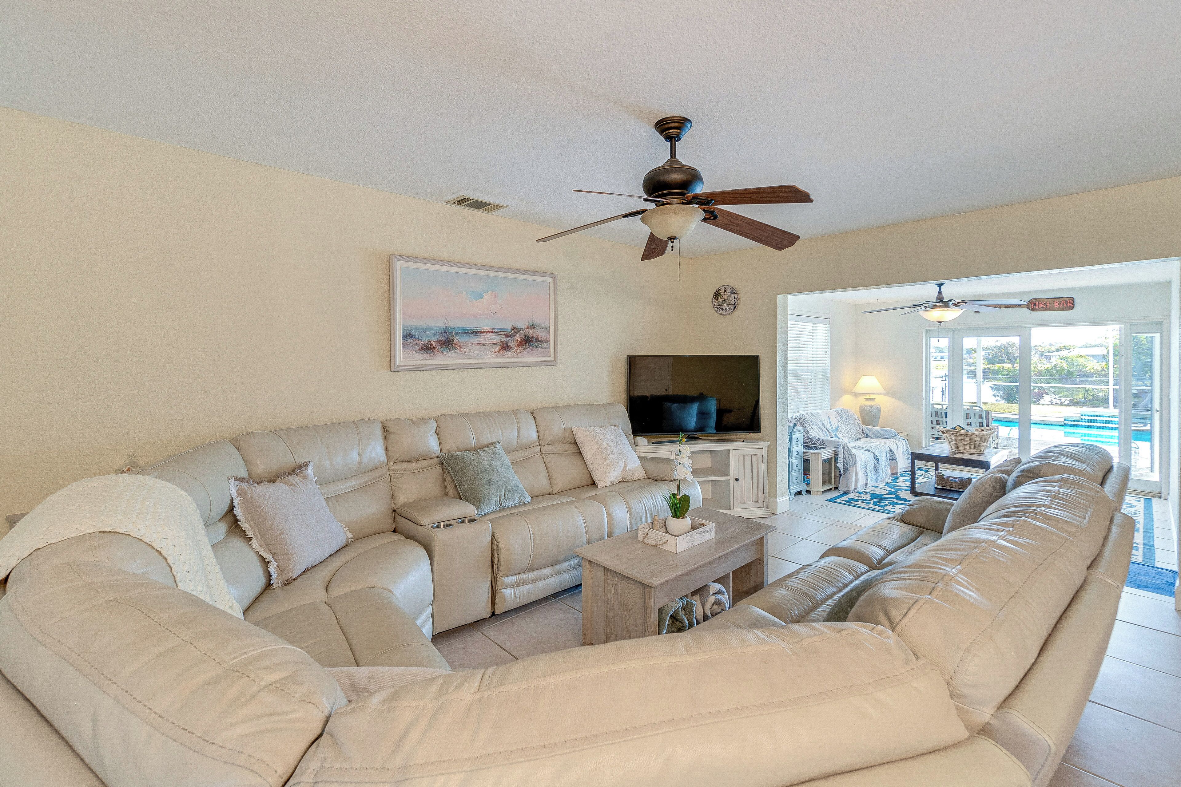A spacious living room with a large beige sectional sofa, a flat-screen TV, and a ceiling fan.