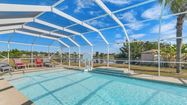 A covered swimming pool with a basketball hoop, red chairs, and a view of the surrounding area.