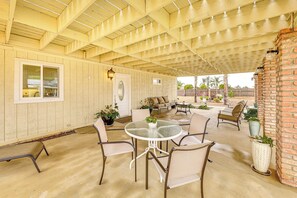 A covered patio area with a round glass table, multiple chairs, and a brick wall. - Patio & Workspace: Peaceful Riverside Retreat! (Riverside)