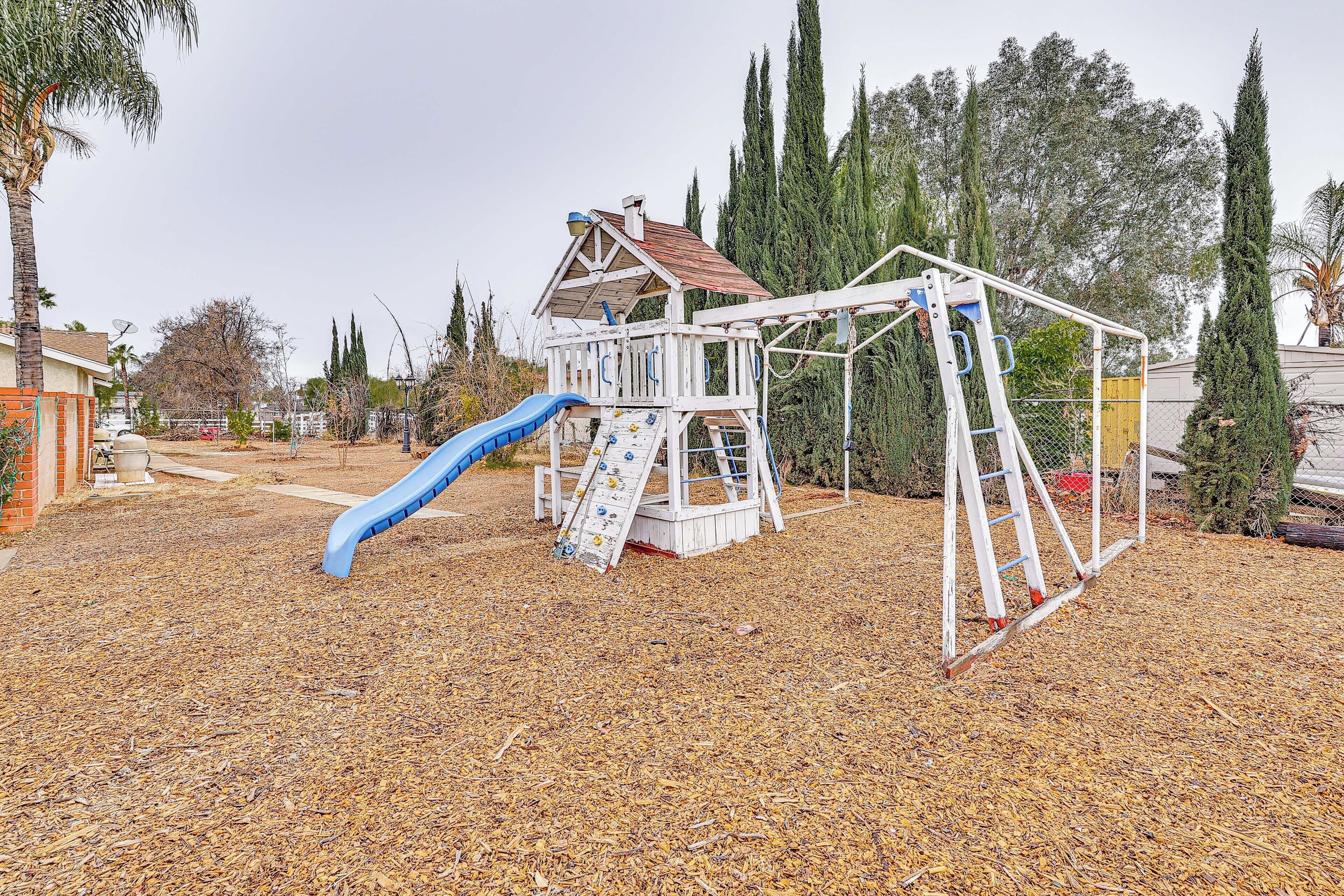 Un'area giochi con scivolo e struttura per arrampicarsi, circondata da alberi e uno strato di pacciamatura asciutta.
