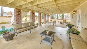 Un área de patio techada al aire libre con una columna de ladrillo, un banco acolchado, una mesa con superficie de vidrio y plantas en macetas.