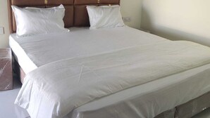 Una cama grande con cabecera marrón y ropa de cama blanca.