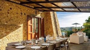An outdoor dining area with stone walls, wooden shutters, and a view of the landscape.