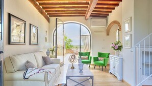 A spacious living room with a sofa, green armchairs, a coffee table, and a view through a large window.