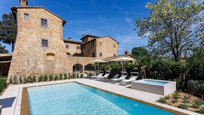 A stone building with a swimming pool, lounge chairs, and umbrellas.