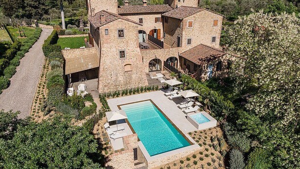 A large stone building with a swimming pool, surrounded by lush greenery and a garden path.