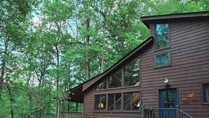Une cabane avec un toit en pente, de grandes fenêtres et une terrasse.
