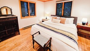 Une chambre avec un plafond en bois, un lit avec une literie à motifs, une table de chevet avec une lampe et une commode.
