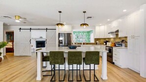 A modern kitchen with white cabinetry, a central island with bar stools, and pendant lighting. - 4 Br Oasis~Pool~Tiki Hut~Hot Tub~Ping Pong~Arcade (Seminole)