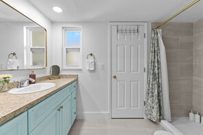 Une salle de bain avec un lavabo blanc, deux porte-serviettes, une porte et un rideau de douche.