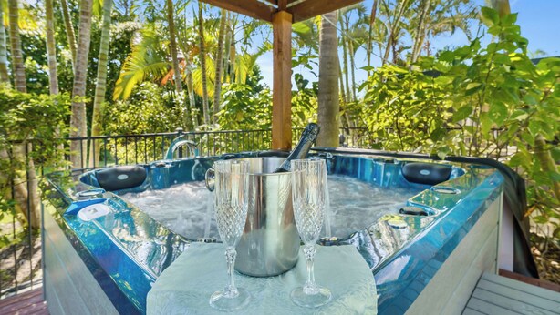 Un jacuzzi con dos copas de cristal sobre una mesa, rodeado de abundante vegetación.