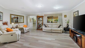 Amplia sala de estar con un televisor de pantalla plana grande, dos sofás de cuero, una mesa de centro de madera y un área de comedor visible a través de una puerta abierta.