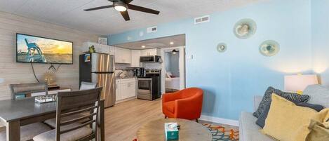 A modern living room with a dining area, a kitchen, and a ceiling fan.