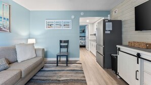 Une cuisine moderne équipée d’un réfrigérateur, d’un four à micro-ondes et d’une cuisinière. On y trouve également un coin repas avec une table et des chaises, ainsi qu’un salon avec un canapé et une lampe.