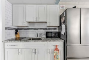 A kitchen with white cabinets, a stainless steel refrigerator, a microwave, and a sink.