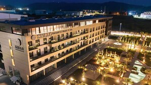 Un hotel de varios pisos con diseño moderno, que cuenta con balcones y un área exterior ajardinada con senderos e iluminación.