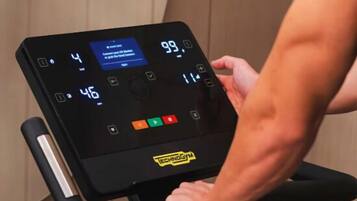 A person using a stationary bike with a digital display and a handlebar.