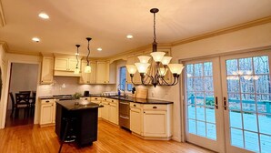 A spacious kitchen with wooden flooring, a central island, and a view through large sliding glass doors.