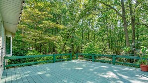 A wooden deck with green railings, surrounded by dense green foliage.