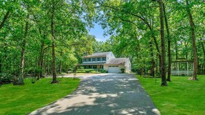 A two-story house with a driveway leading to the garage, surrounded by lush green trees.