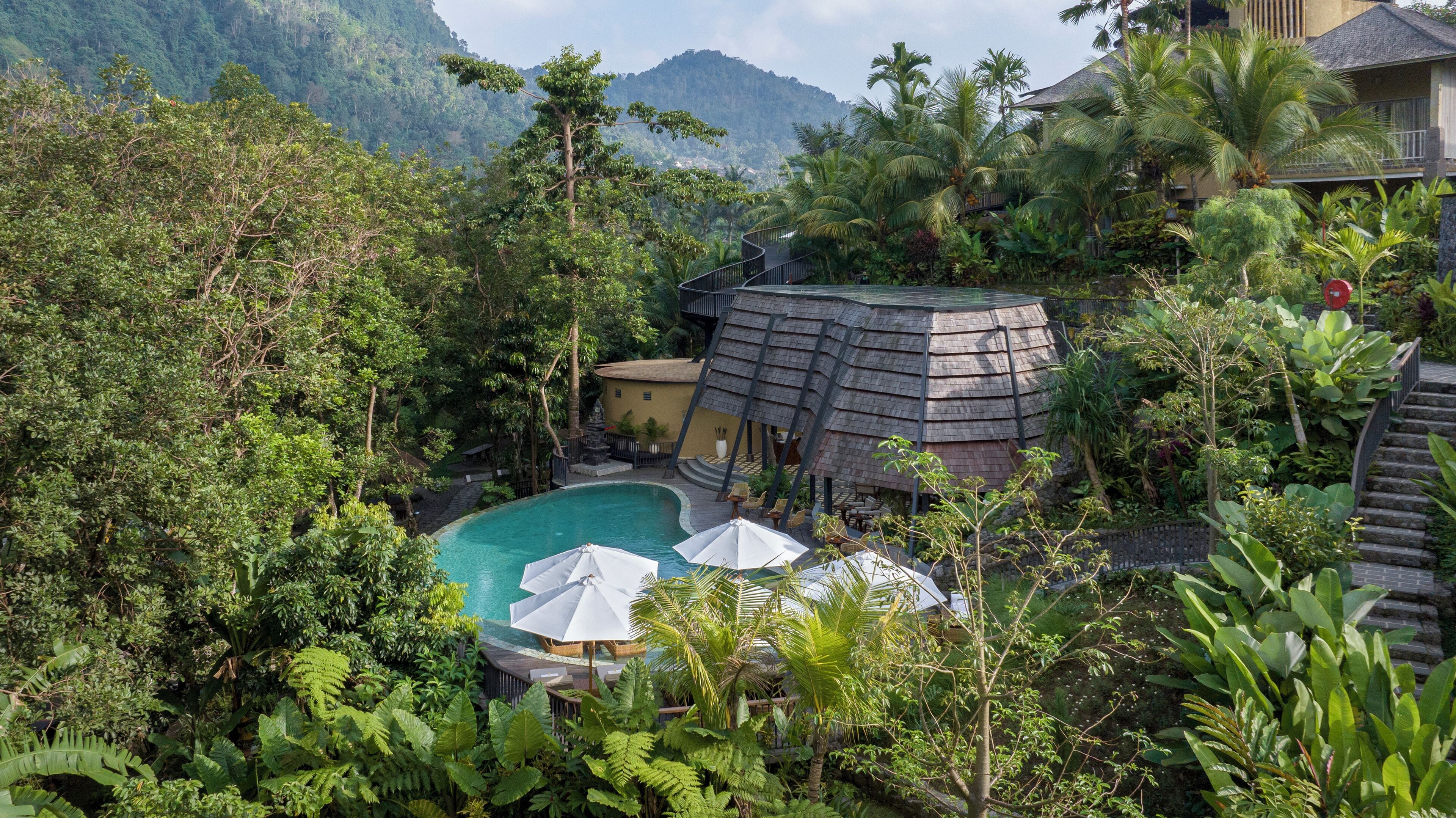A tropical resort with a swimming pool surrounded by lush greenery and a mountain backdrop.