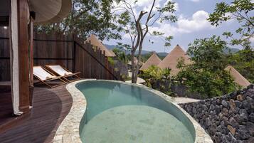 A swimming pool with a wooden deck and lounge chairs, surrounded by a stone wall and trees.