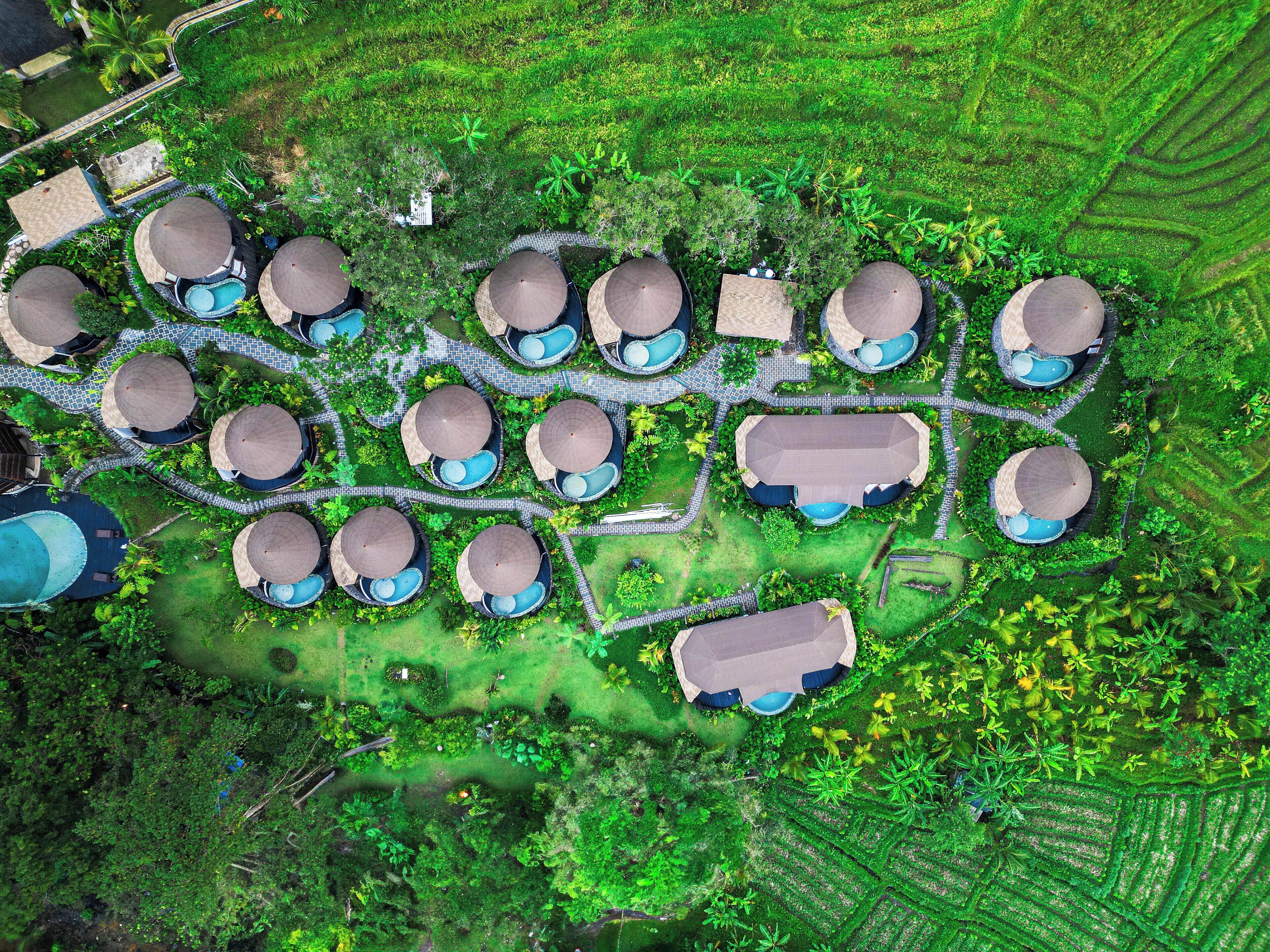 An aerial view of a resort with multiple bungalow-style accommodations, each with a thatched roof and a small pool.