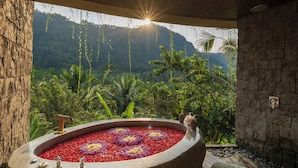 A spa area with a hot tub surrounded by red and purple flowers, a stone wall, and a view of lush greenery and mountains. - The Wapa Lux Tent (Sidemen)