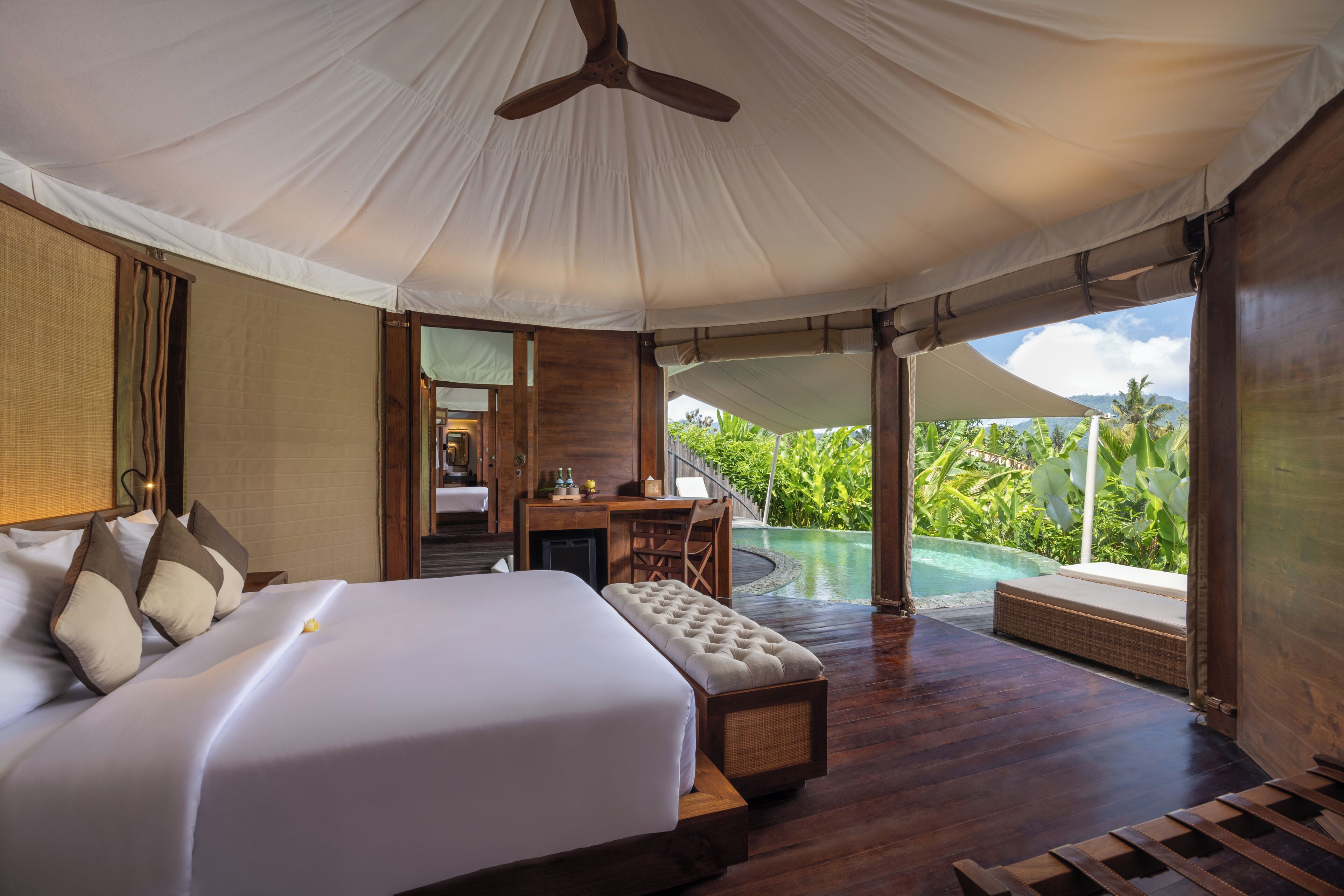 A spacious bedroom with a large bed, a desk, and a view of an infinity pool.