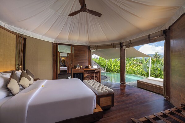 A spacious bedroom with a large bed, a desk, and a view of an infinity pool. - The Wapa Lux Tent (Sidemen)