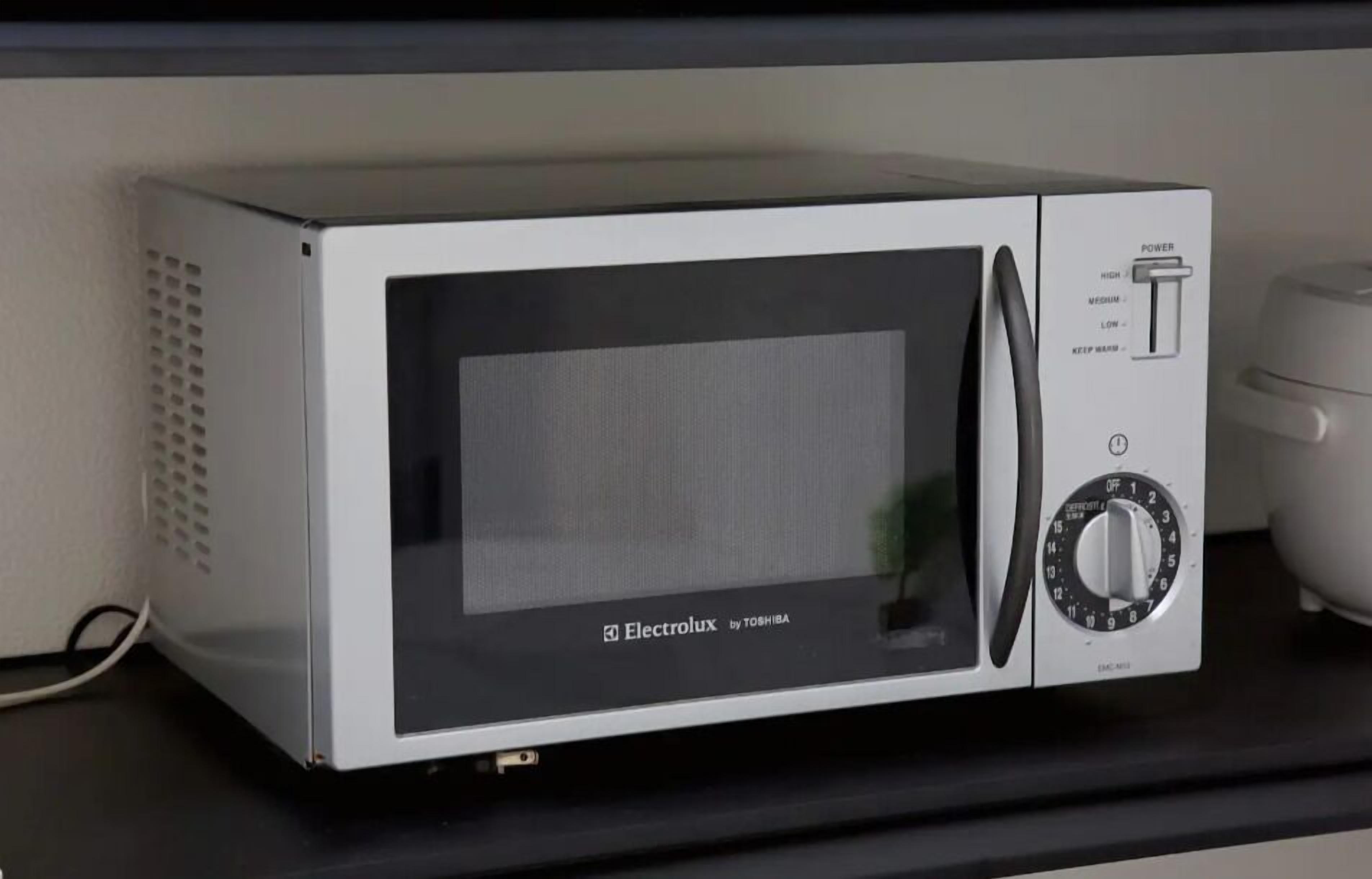 Un horno microondas con pantalla digital y panel de control, sobre una encimera negra.