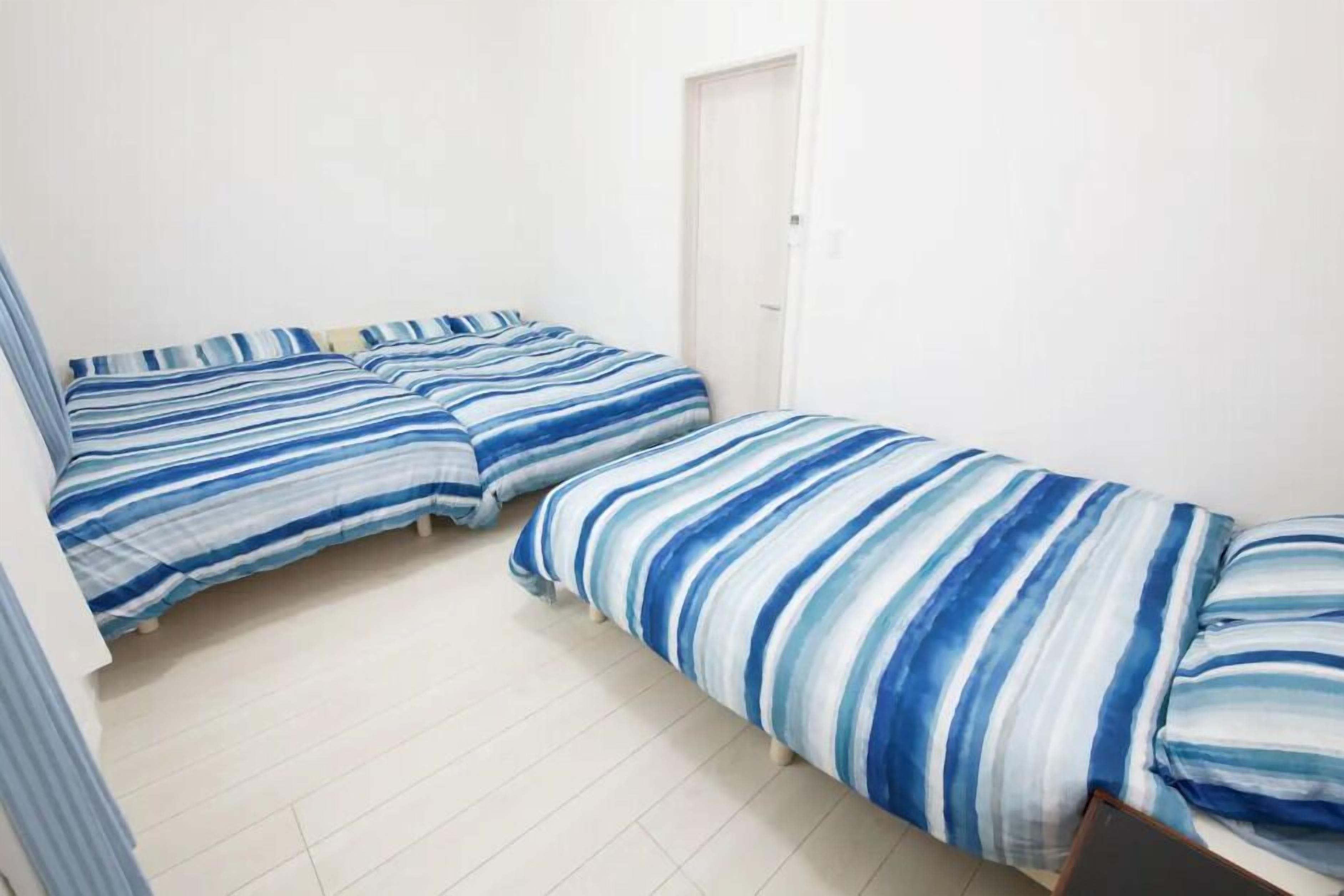 A room with two beds, each with striped bedding, a white door, and a tiled floor.