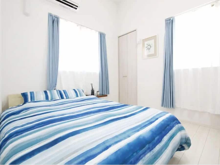 A bedroom with a bed, a nightstand, a framed picture on the wall, and a window with curtains.