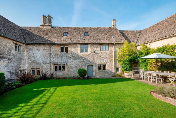 A stone building with a courtyard, a dining area with outdoor seating, and a well-maintained lawn.