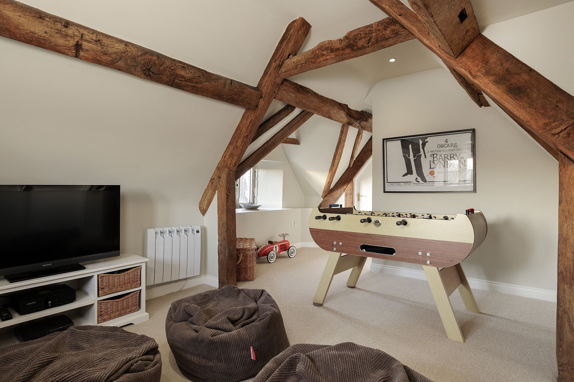 Ein gemütliches Loft-Zimmer mit freiliegenden Holzbalken, einem Tischkicker, einem Fernseher und einer gemütlichen Sitzecke.
