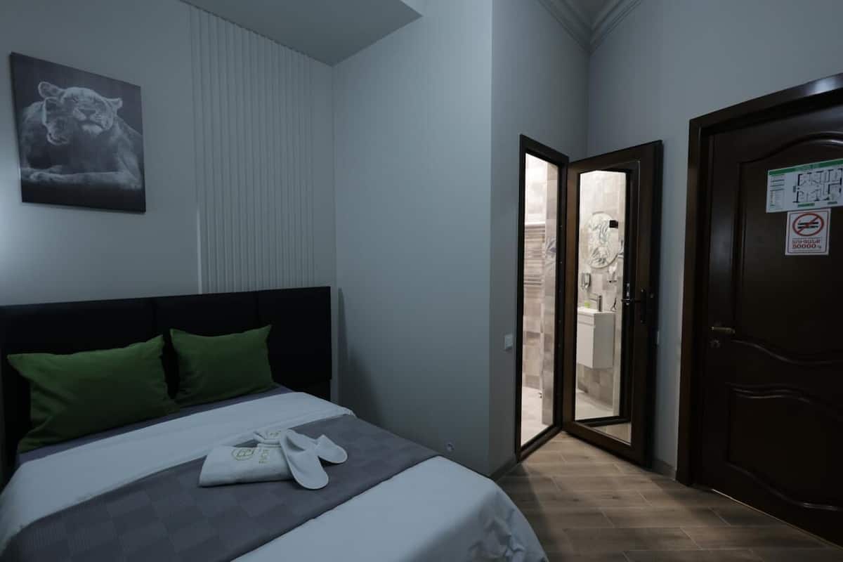 A hotel room with a bed, green pillows, a towel, and a pair of slippers.